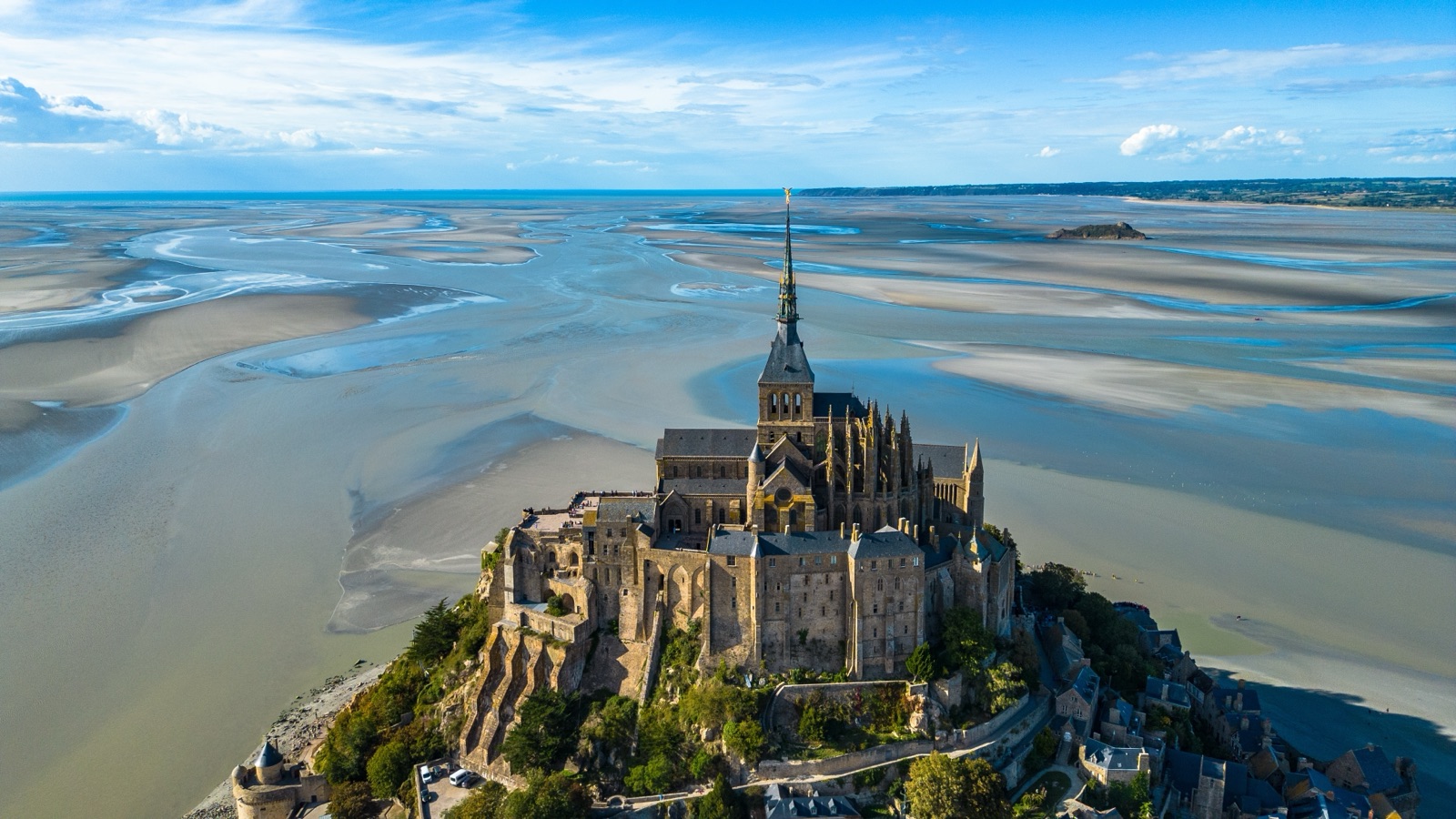 Aerial view of the abbey and spire of Mont-Saint-Michel above the sandbanks and channels of the bay at low tide
