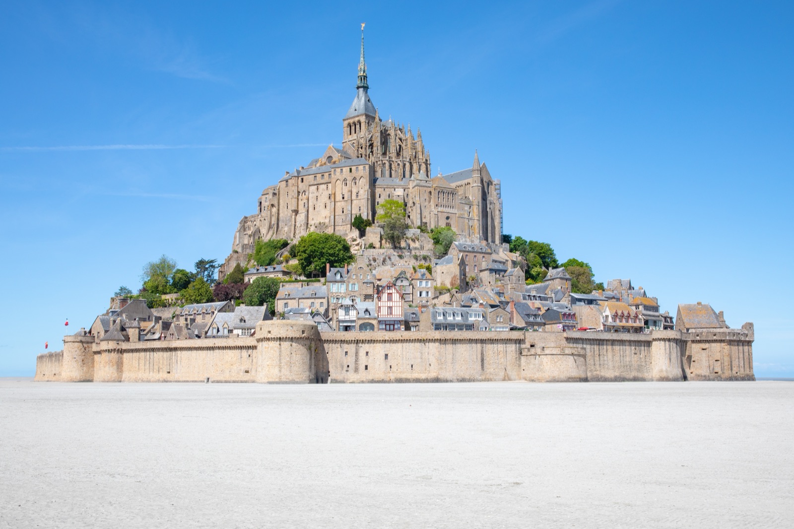 The ramparts, village houses and abbey of Mont-Saint-Michel seen from the sands under a clear blue sky